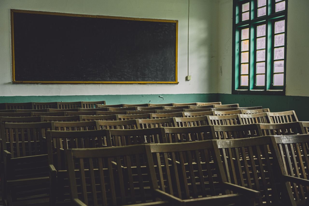 creative-01 Empty vintage classroom with wooden chairs, large blackboard, and windows.